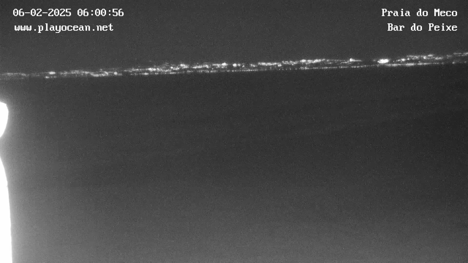 A nighttime, low-light view shows a faint line of lights on the horizon over a dark body of water.
