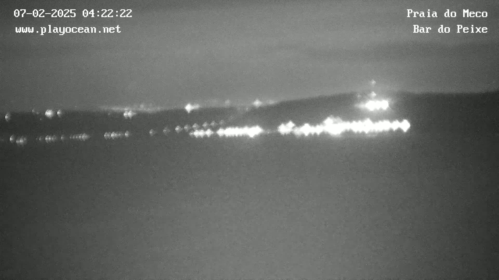 A nighttime, low-light image shows a line of lights on the horizon, possibly from a distant town or coastline.