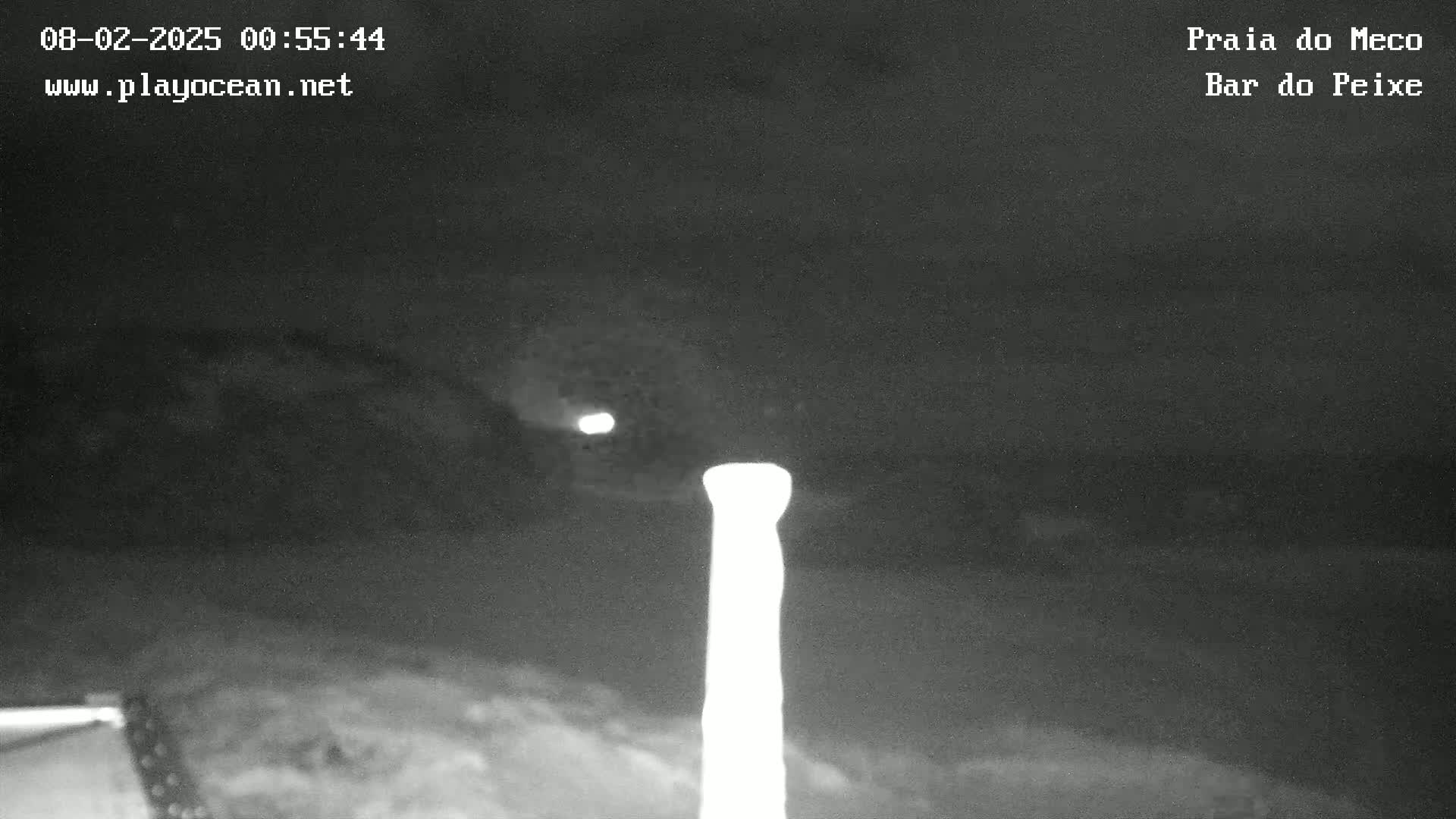 A nighttime, low-light image shows a tall, thin, bright object in the center, with a dark, cloudy sky and dimly lit land in the background.