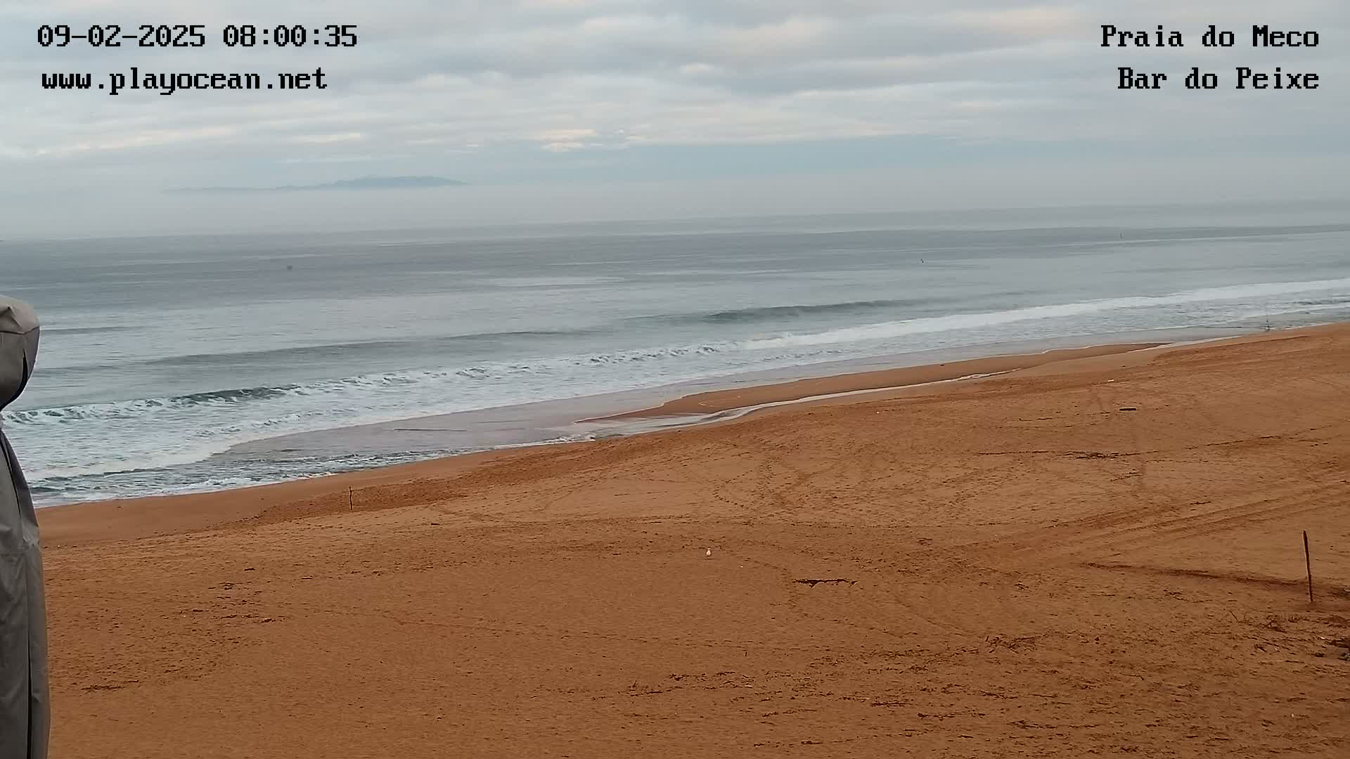 A sandy beach slopes down to a calm ocean under an overcast sky.