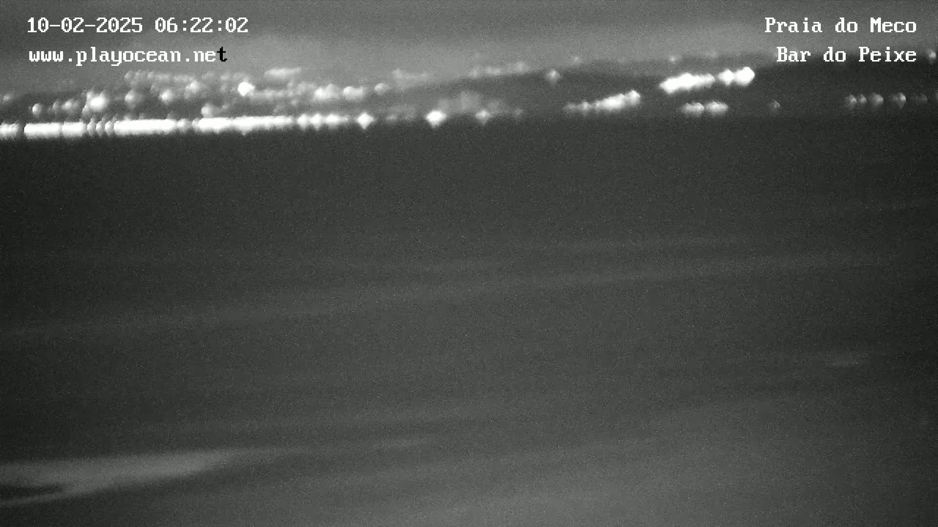 A nighttime, low-light image shows a dark body of water with a distant, faintly lit shoreline.