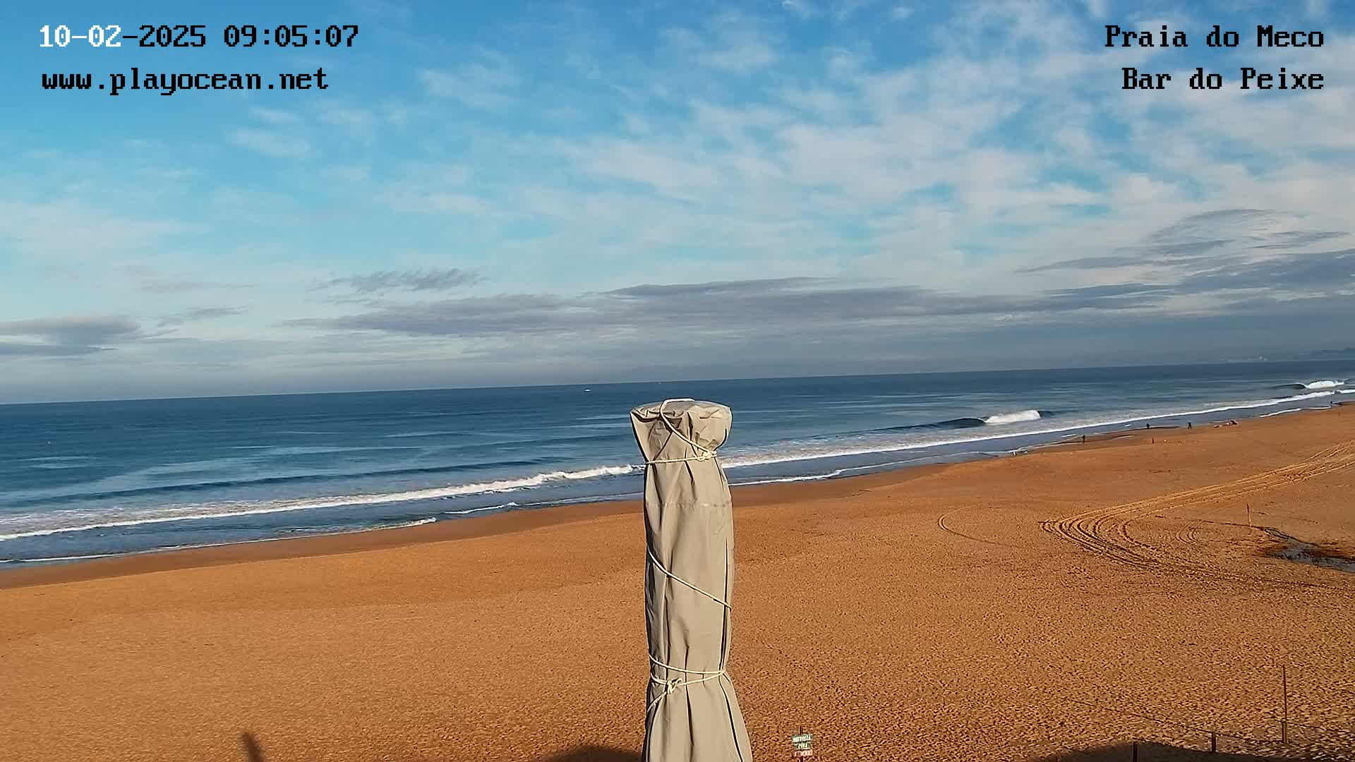 A sandy beach stretches towards a blue ocean with small waves under a partly cloudy sky.