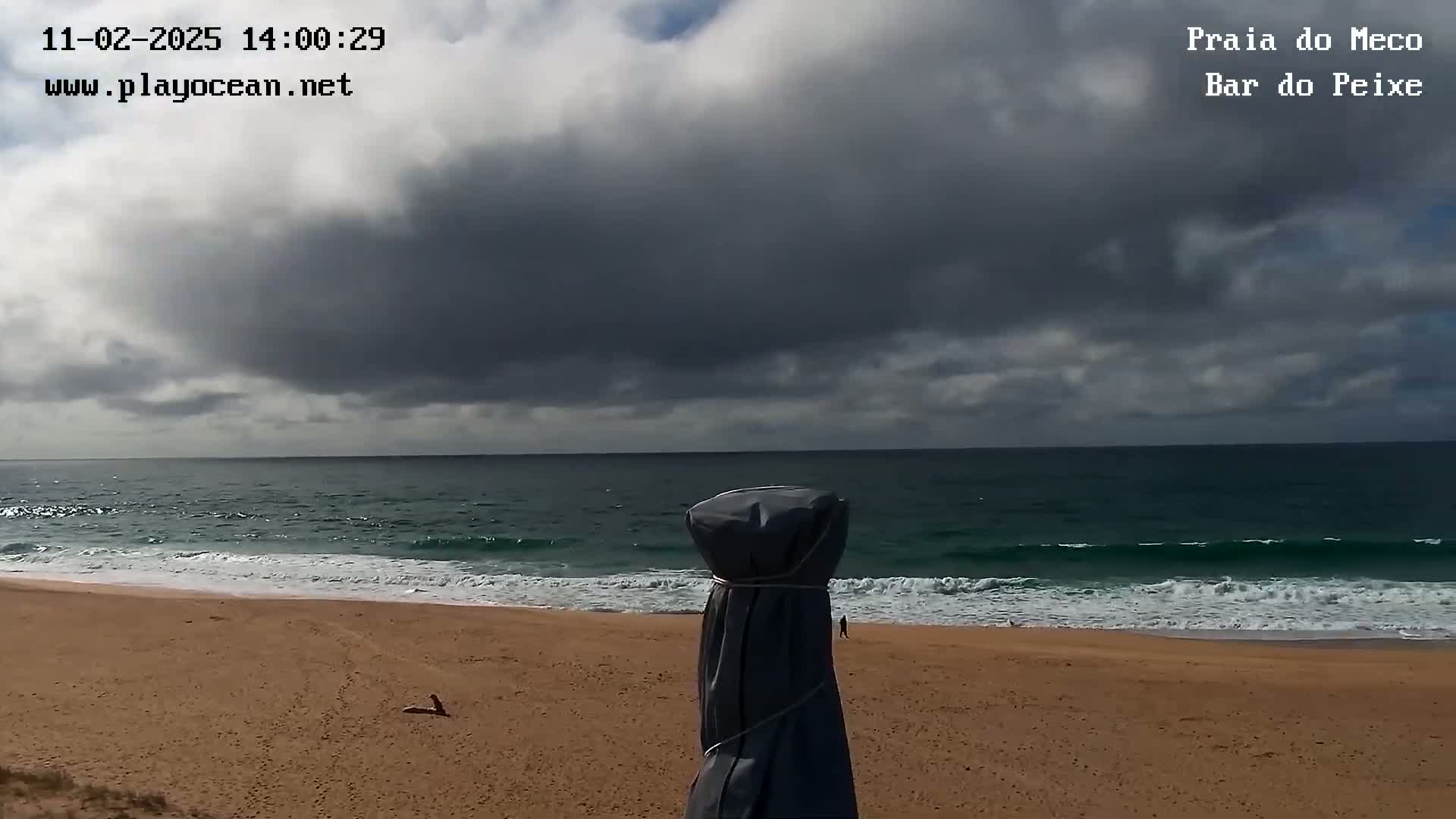 A sandy beach with small waves under a mostly cloudy sky.