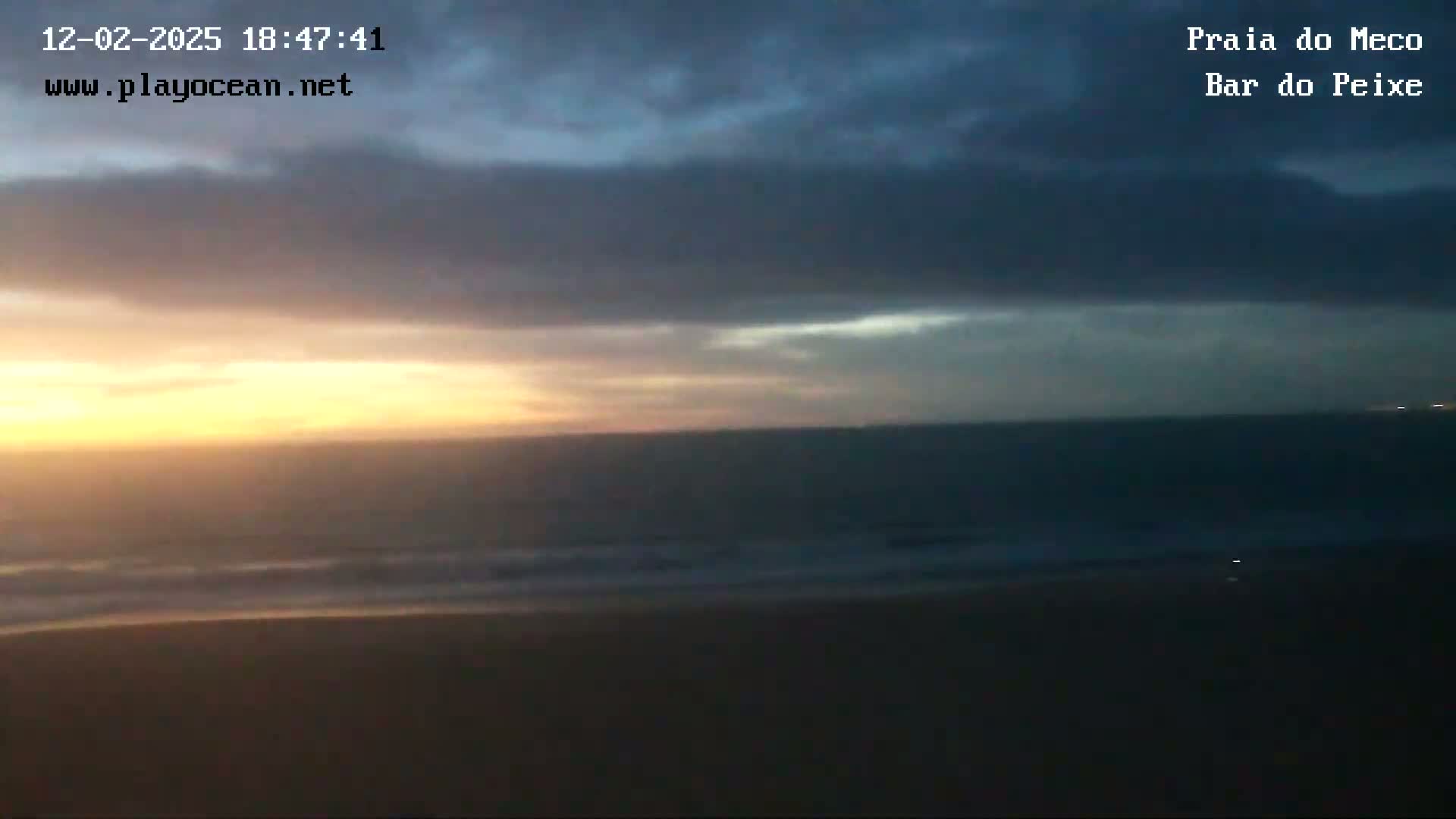A dark, cloudy sunset over a calm ocean and sandy beach.
