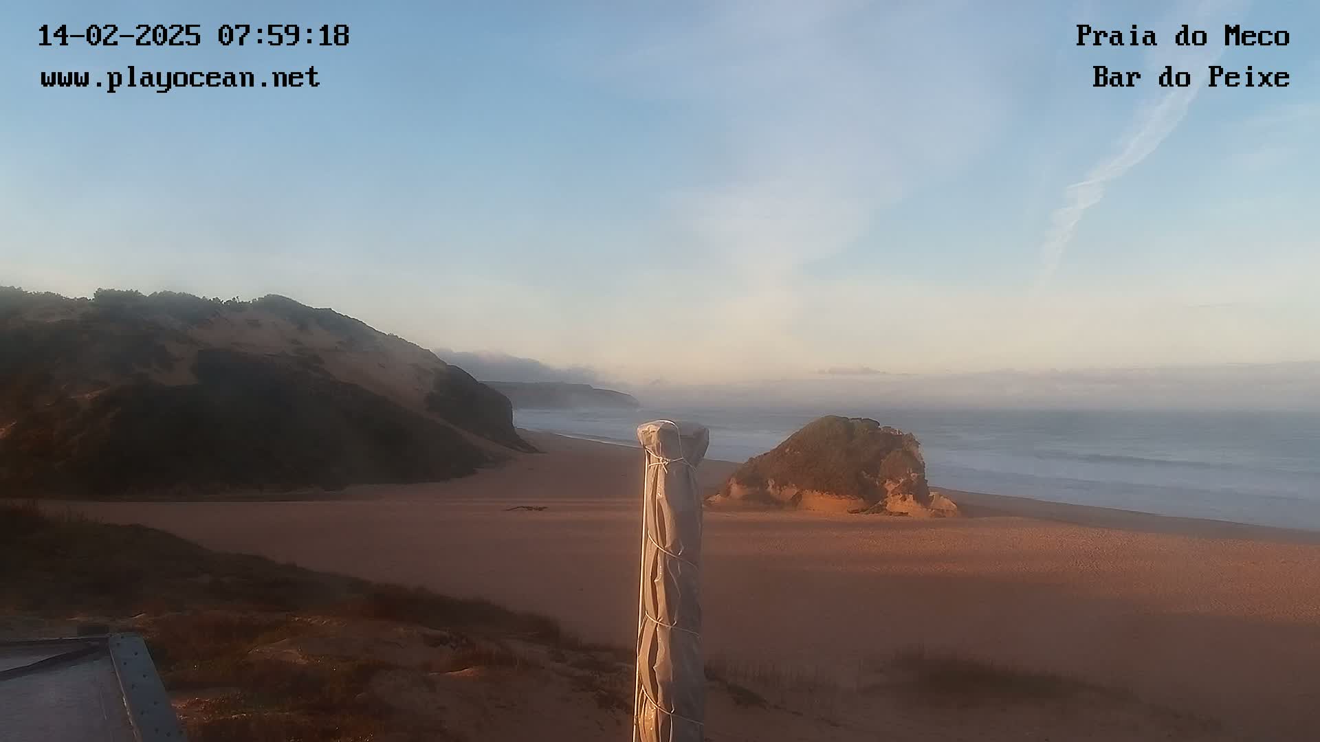 A sandy beach with low cliffs and a calm ocean under a clear, light-blue sky.