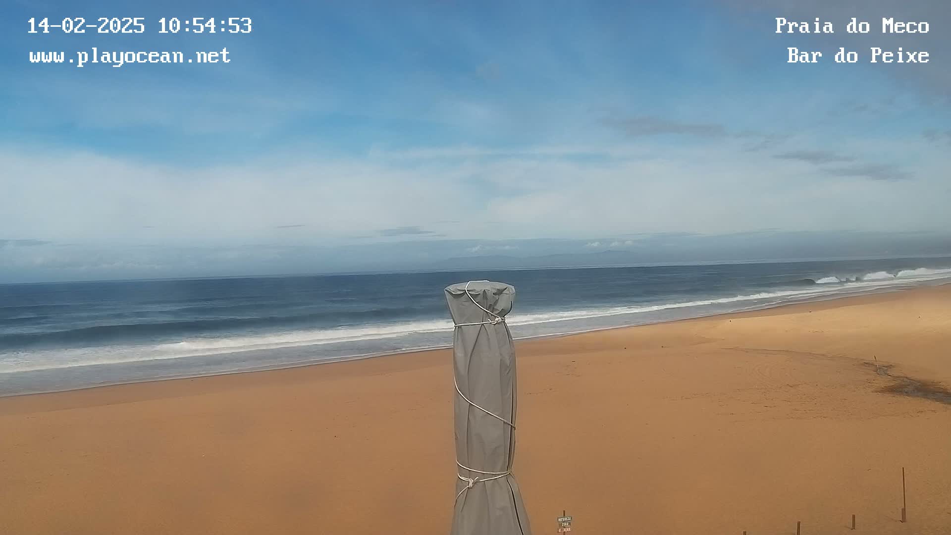 A mostly sunny day at a beach shows a gently rolling ocean meeting a wide sandy shore, with a covered object standing in the foreground.