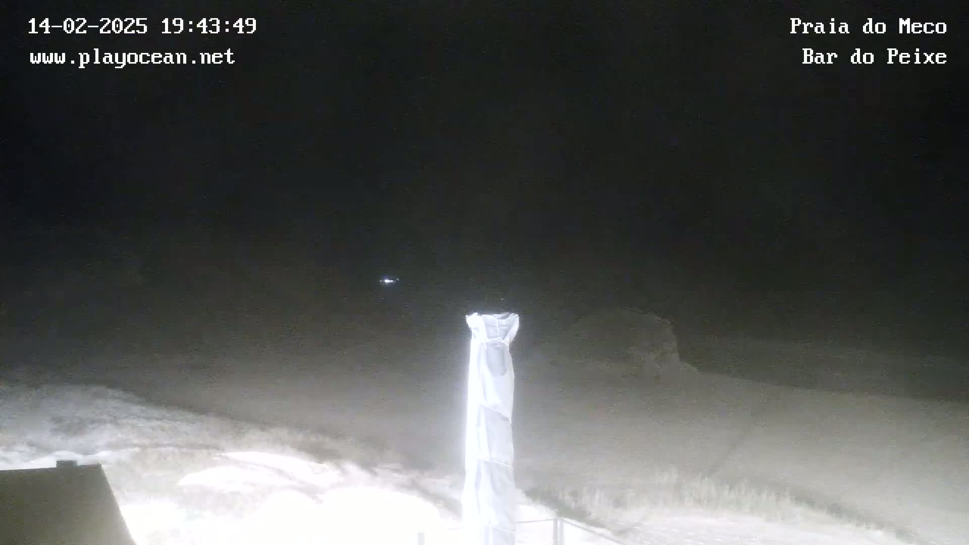 A nighttime, dimly lit outdoor scene shows a white, fabric-covered object standing near a snow-covered slope under a dark, cloudy sky.