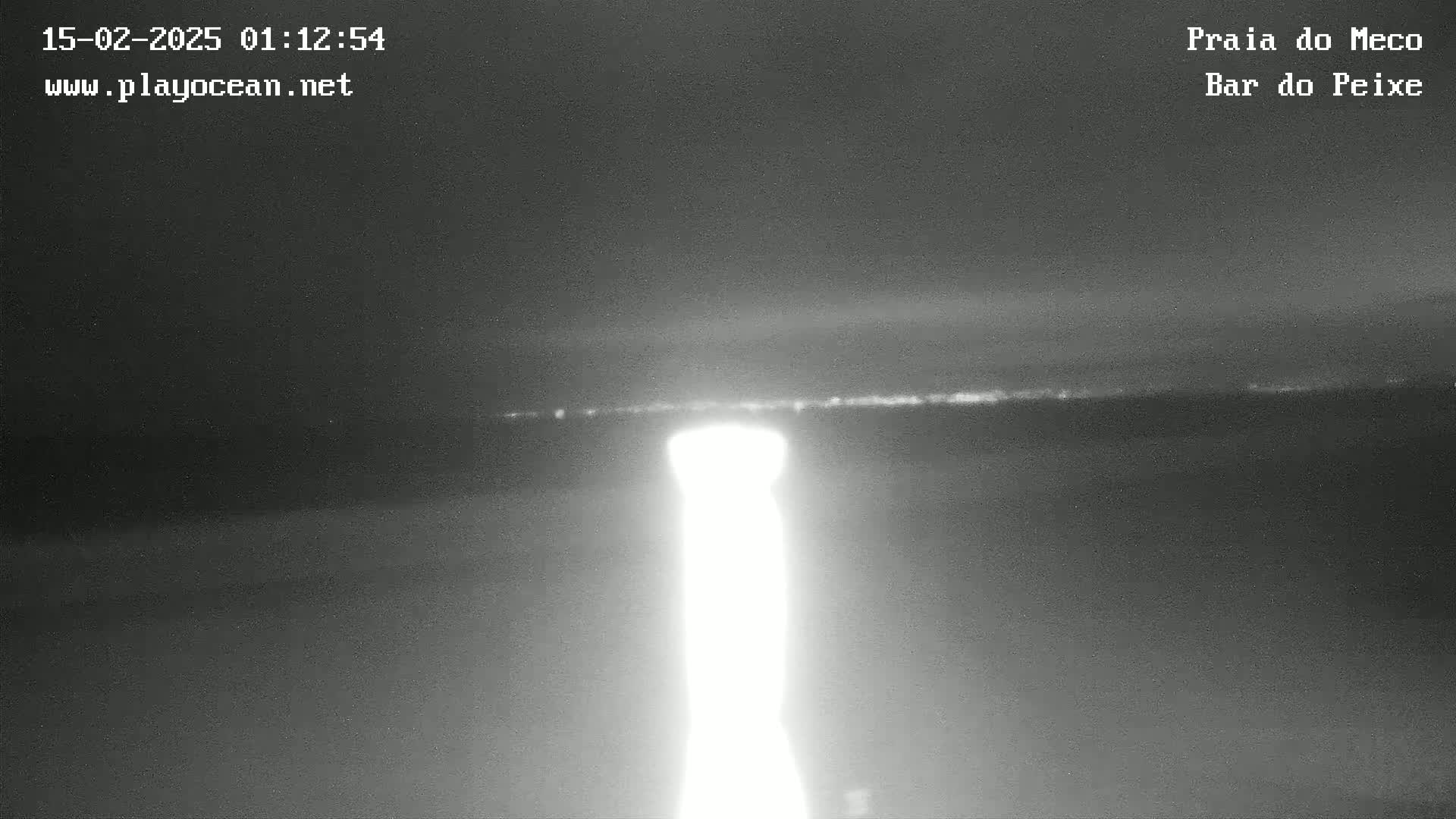 A bright light shines from the bottom of the frame toward a dark, flat horizon under a night sky.
