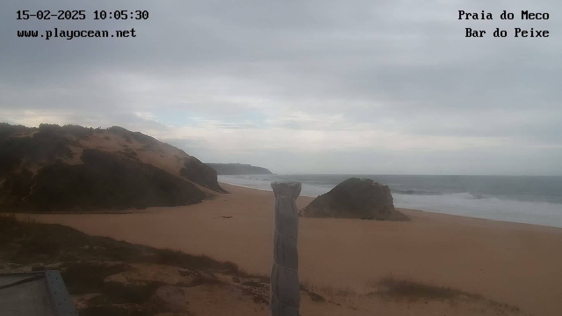A sandy beach with dark-colored cliffs and a gray, overcast sky stretches to a wavy ocean.