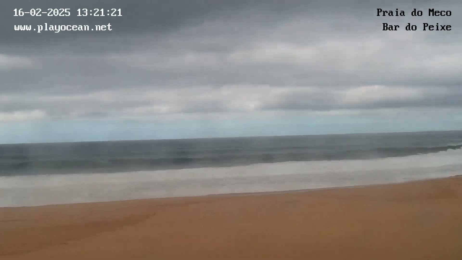 A sandy beach stretches out to a dark-grey ocean under a cloudy sky.