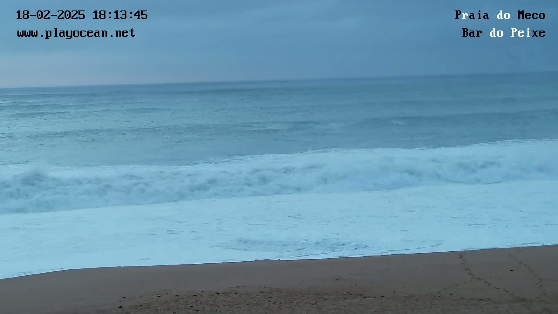 Under an overcast sky, moderate waves crash onto a sandy beach.