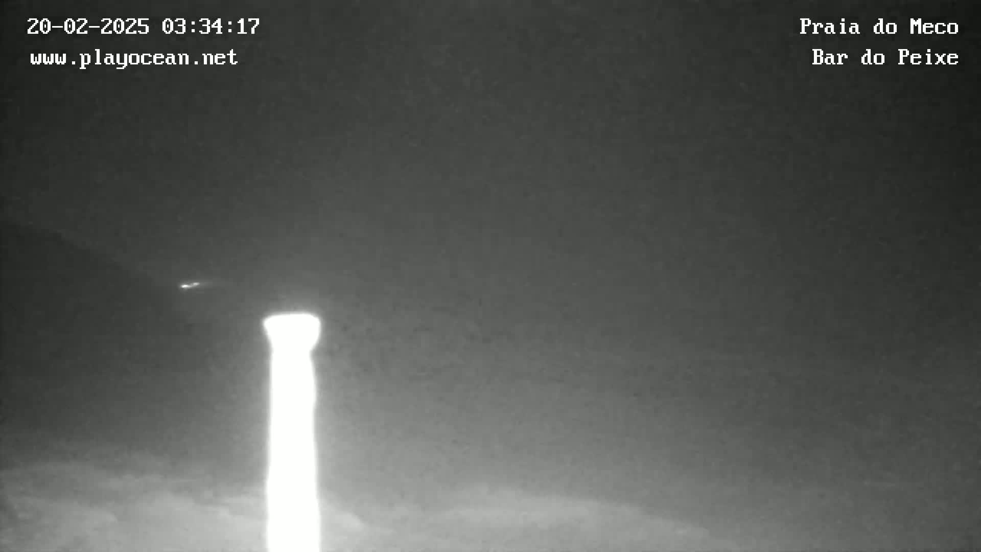 A brightly lit, tall, thin object stands in the center of a dark, nighttime scene.