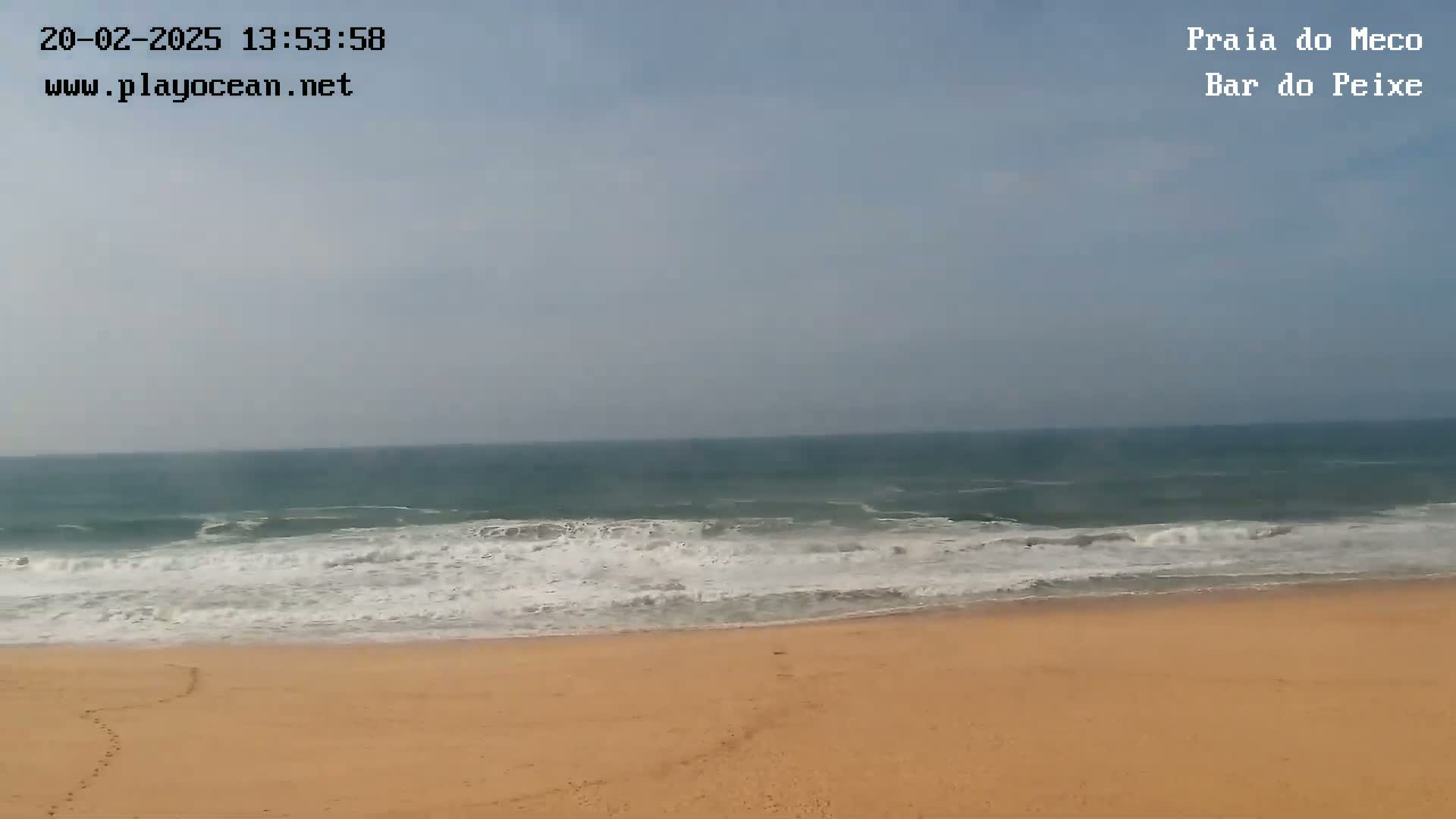 A sandy beach with moderately sized waves rolling onto the shore under a mostly cloudy sky.