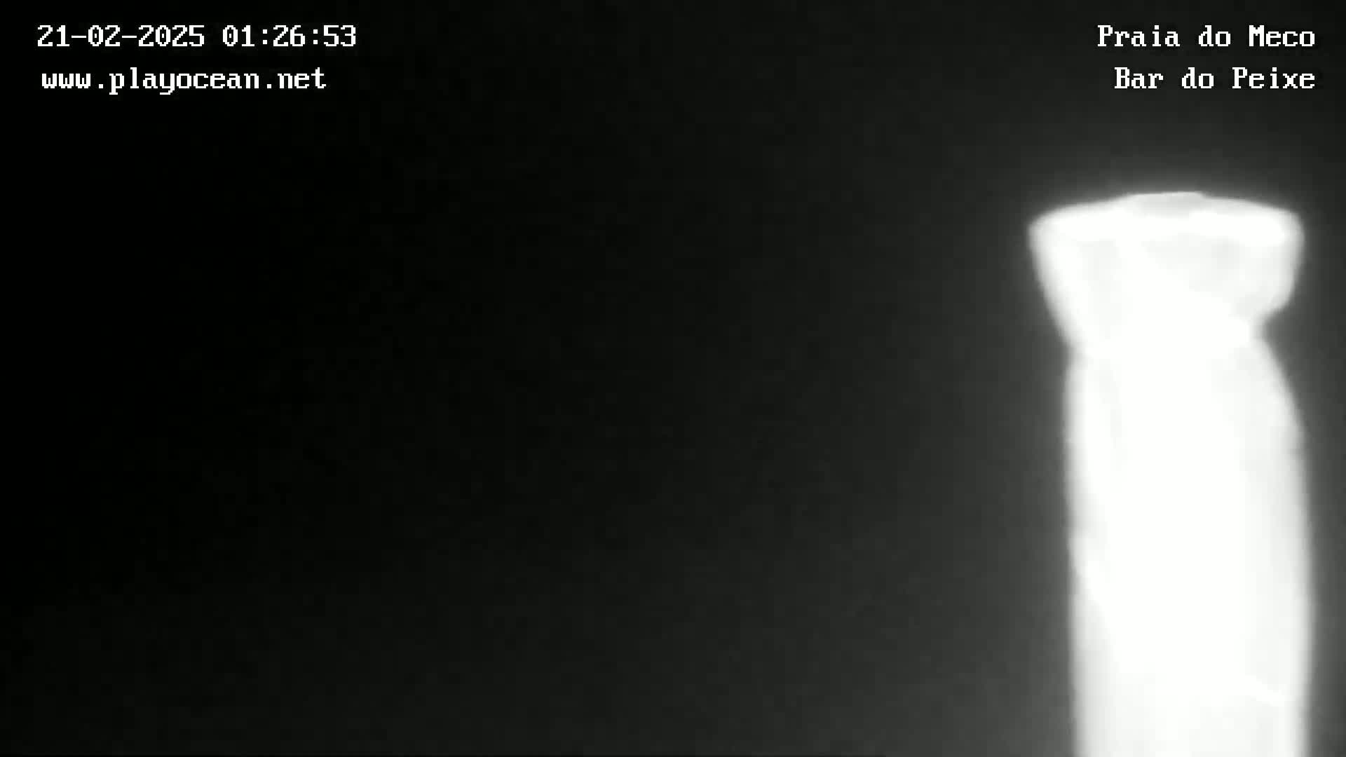 A brightly lit, tall, thin, indistinct object stands out against a dark, nighttime background.