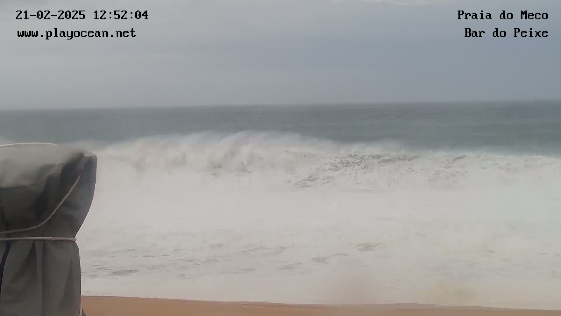 Large waves crash on a sandy beach under an overcast sky.