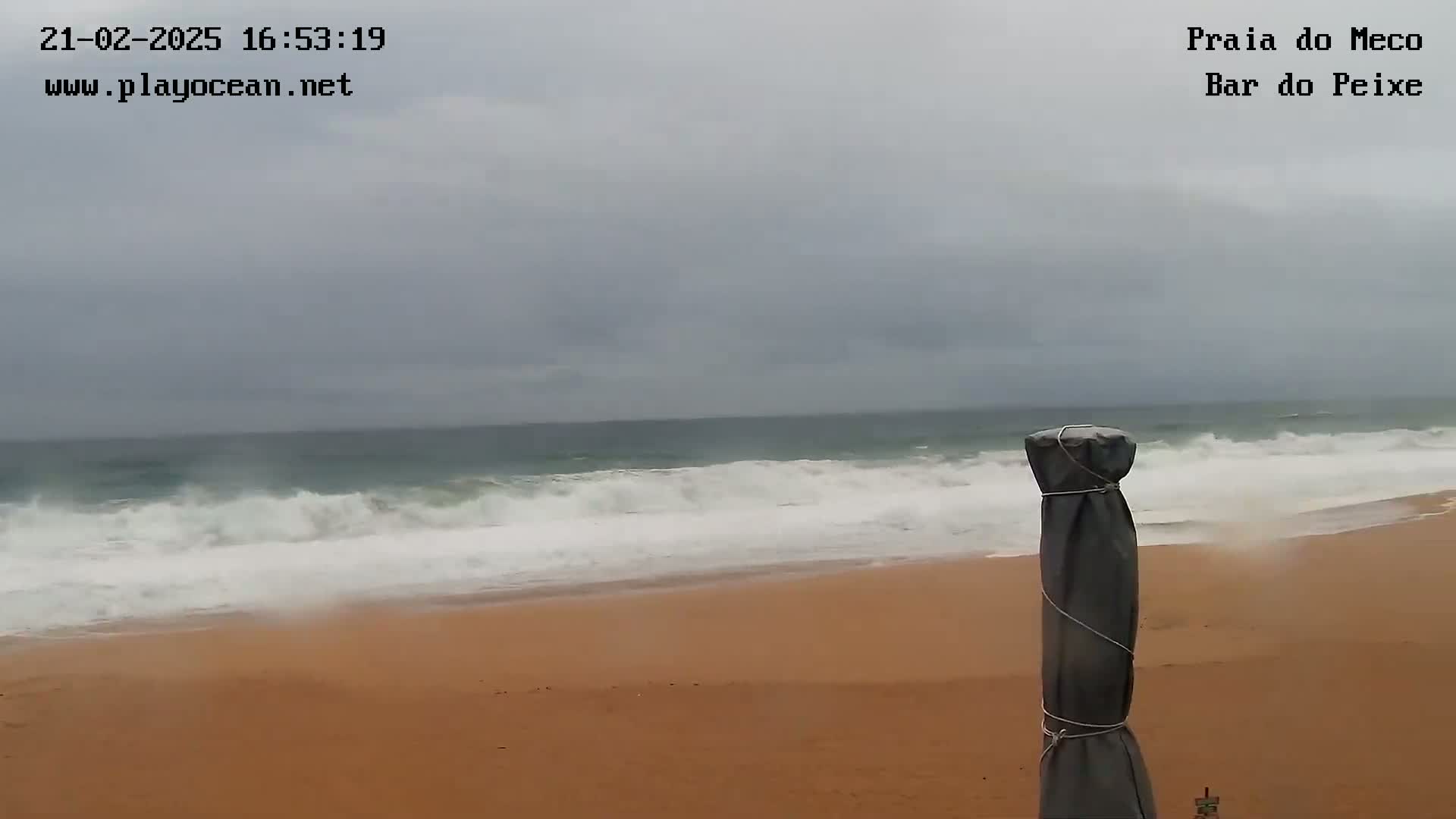 A sandy beach with moderate waves crashing on the shore under an overcast sky.