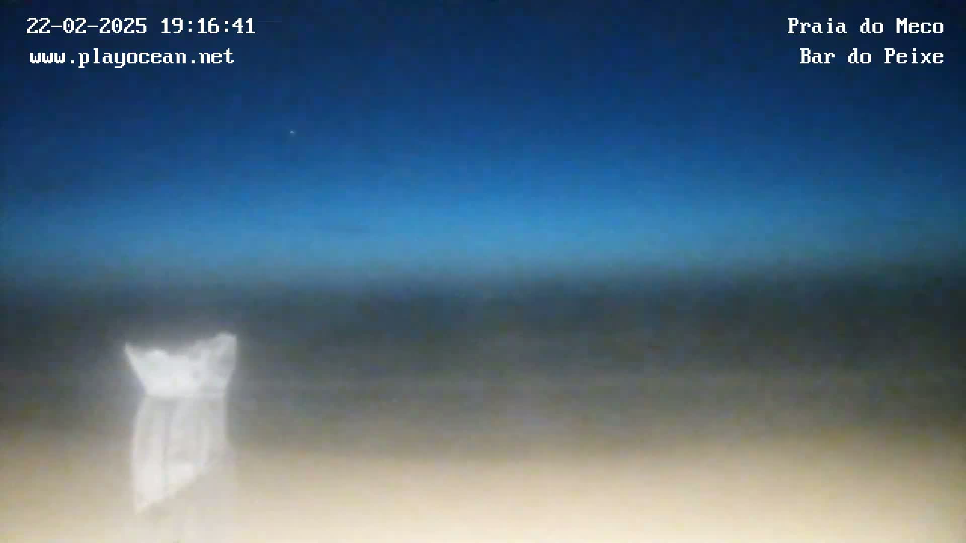 A blurry image shows a dark-blue twilight sky over a beach with a white, indistinct object in the foreground.