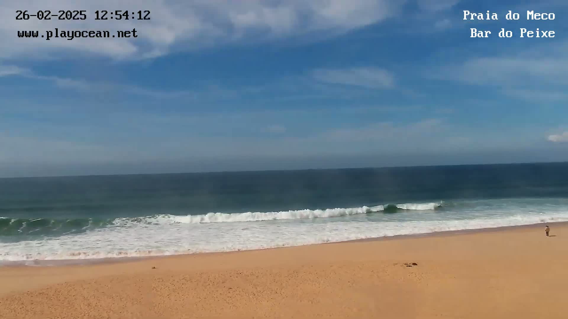 A sandy beach with gently rolling waves under a mostly sunny sky.