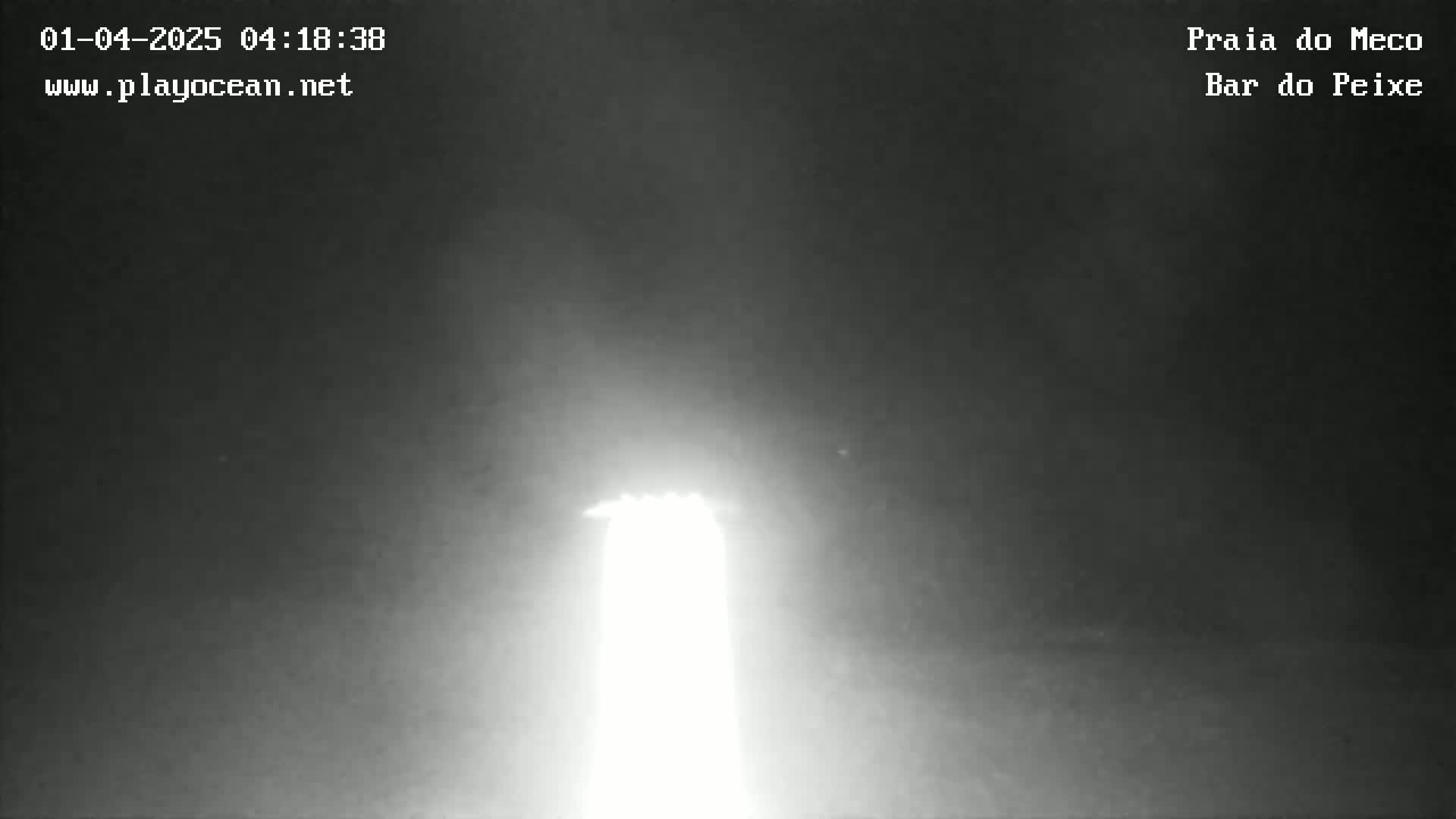 A bright light, possibly a lighthouse, is visible in the dark, hazy night.