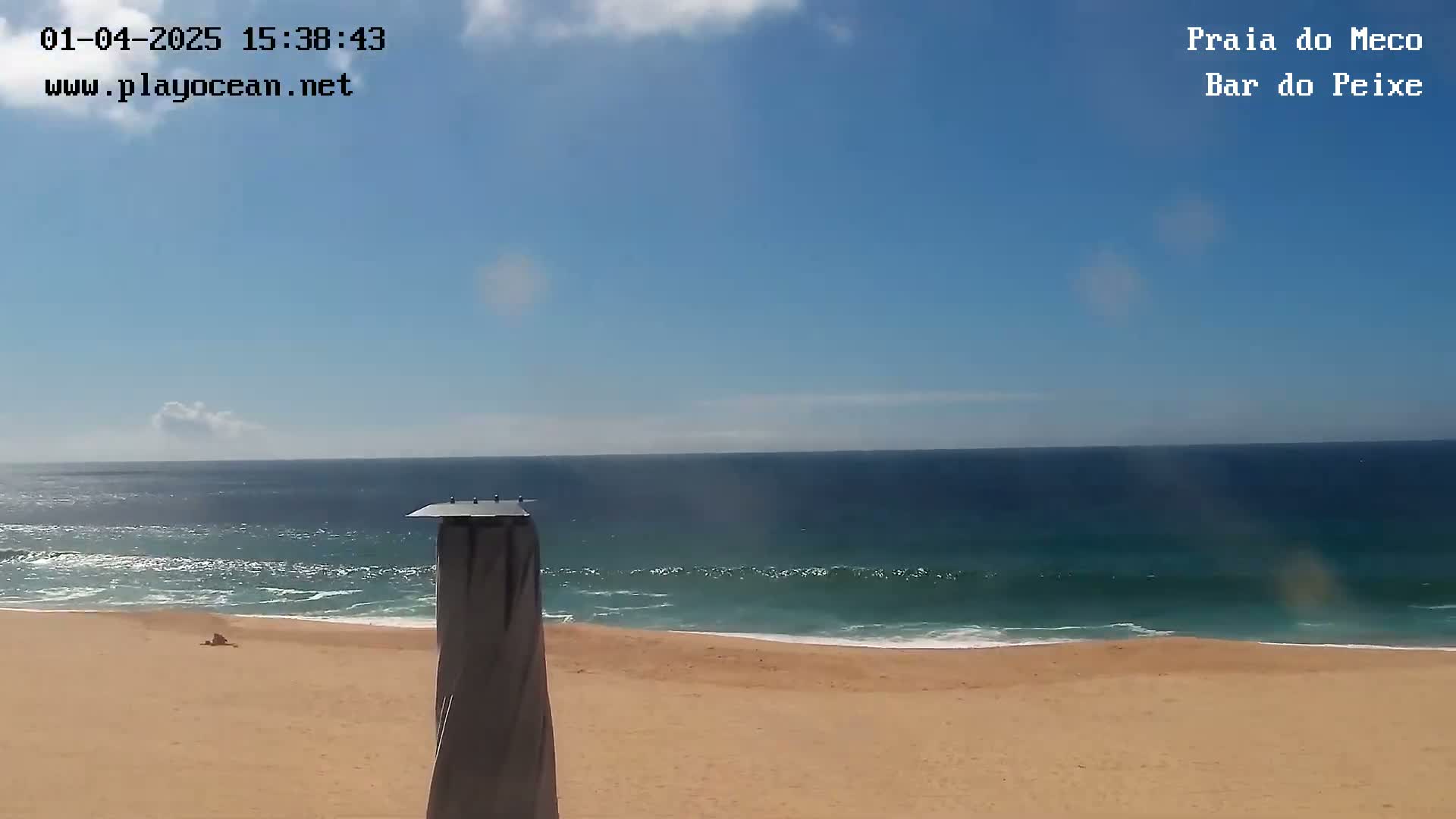 A mostly sunny day at a sandy beach shows a calm ocean with small waves.