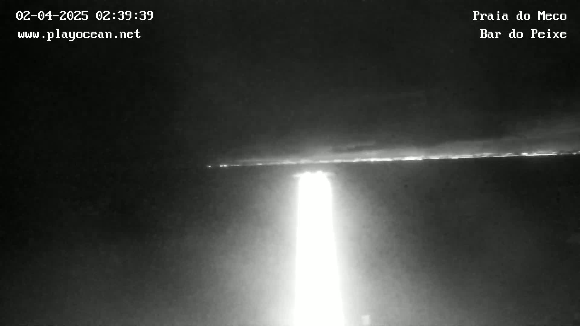 A bright light shines upward from a dark body of water under a mostly clear night sky.
