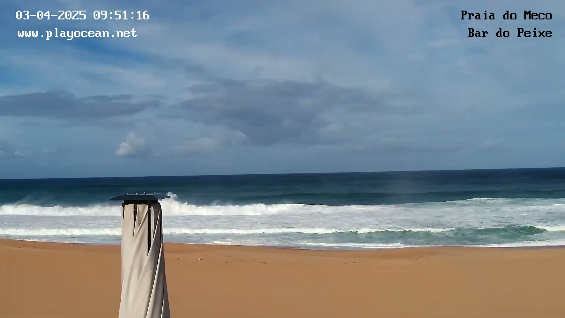 A sandy beach with moderate waves rolling onto the shore under a partly cloudy sky.