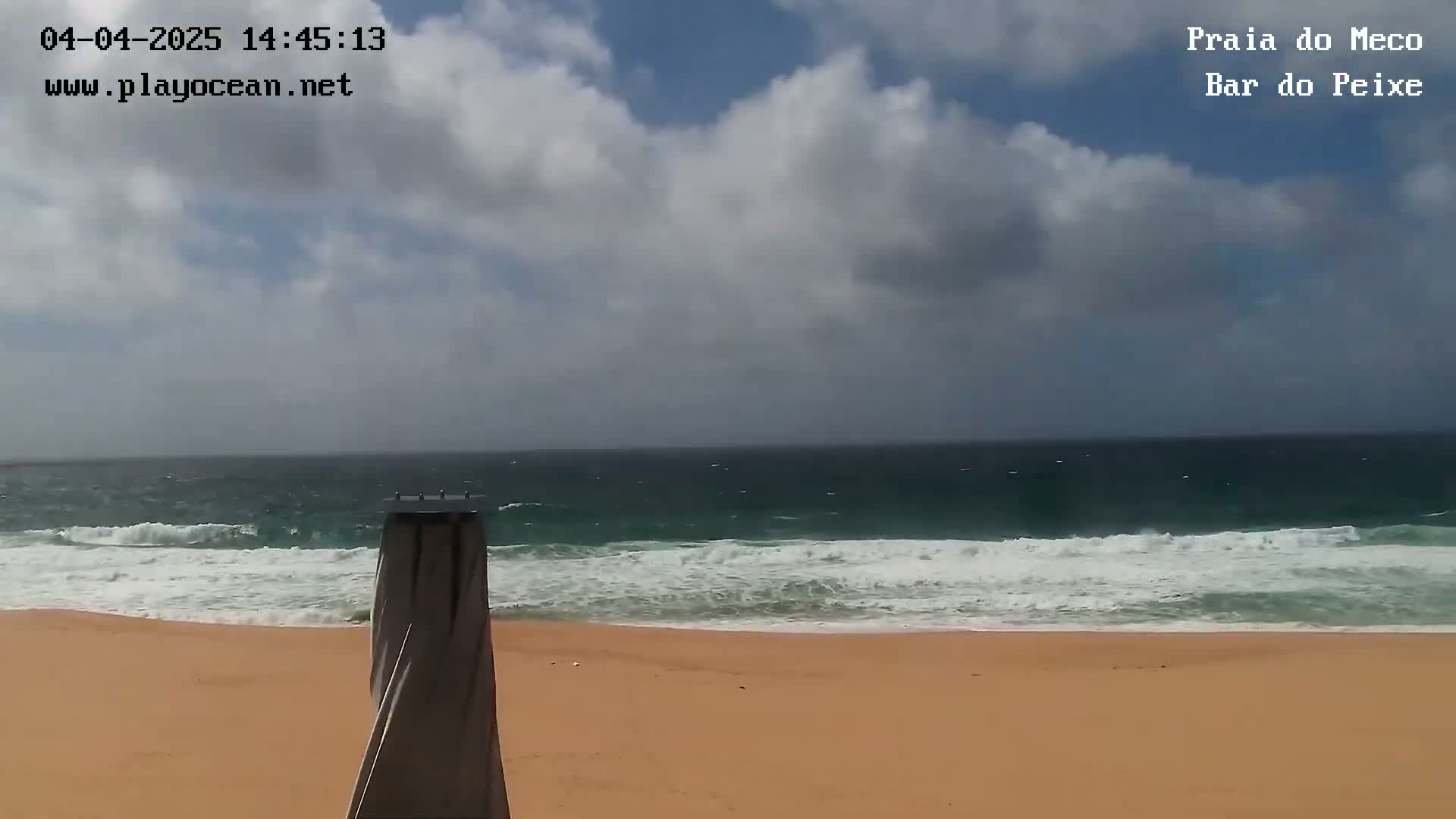 A partly cloudy day shows a sandy beach and ocean with moderate waves.