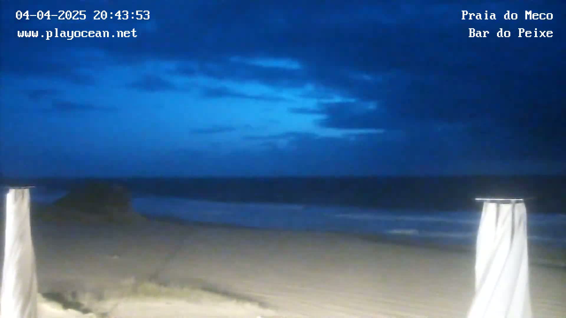 A dark-blue, twilight sky overlooks a calm ocean and sandy beach.