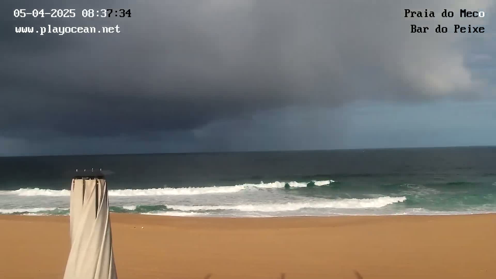 A sandy beach with gentle waves under a dark, cloudy sky.