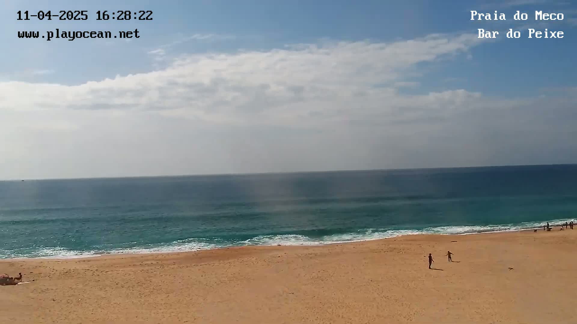 A sandy beach stretches to a teal ocean under a partly cloudy sky.