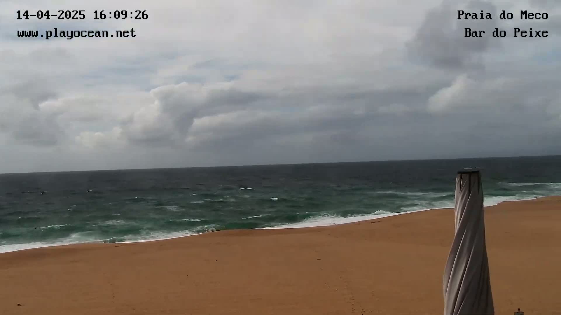 A sandy beach meets a dark-green ocean under a mostly cloudy sky.