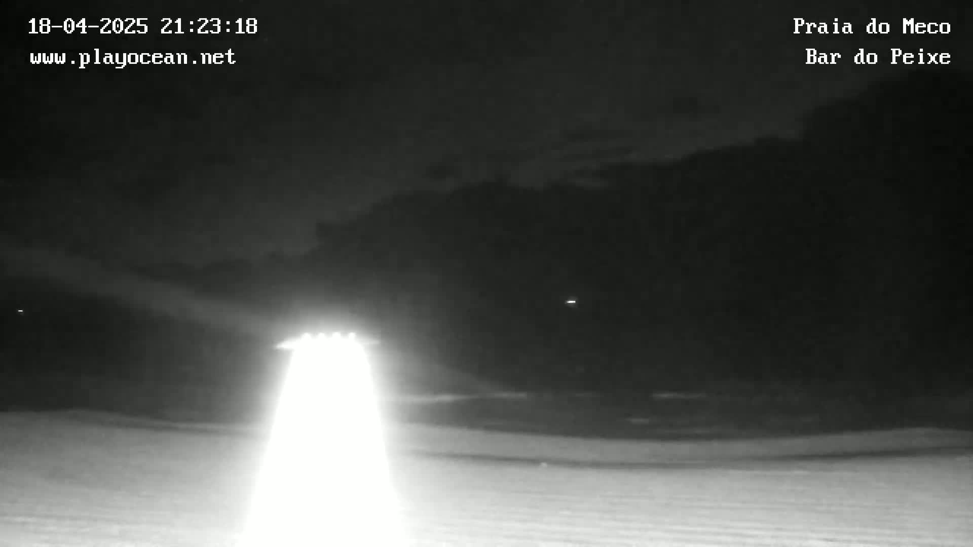 A nighttime, low-light image shows a flat, snow-covered expanse under a dark, cloudy sky, illuminated by bright lights in the foreground.