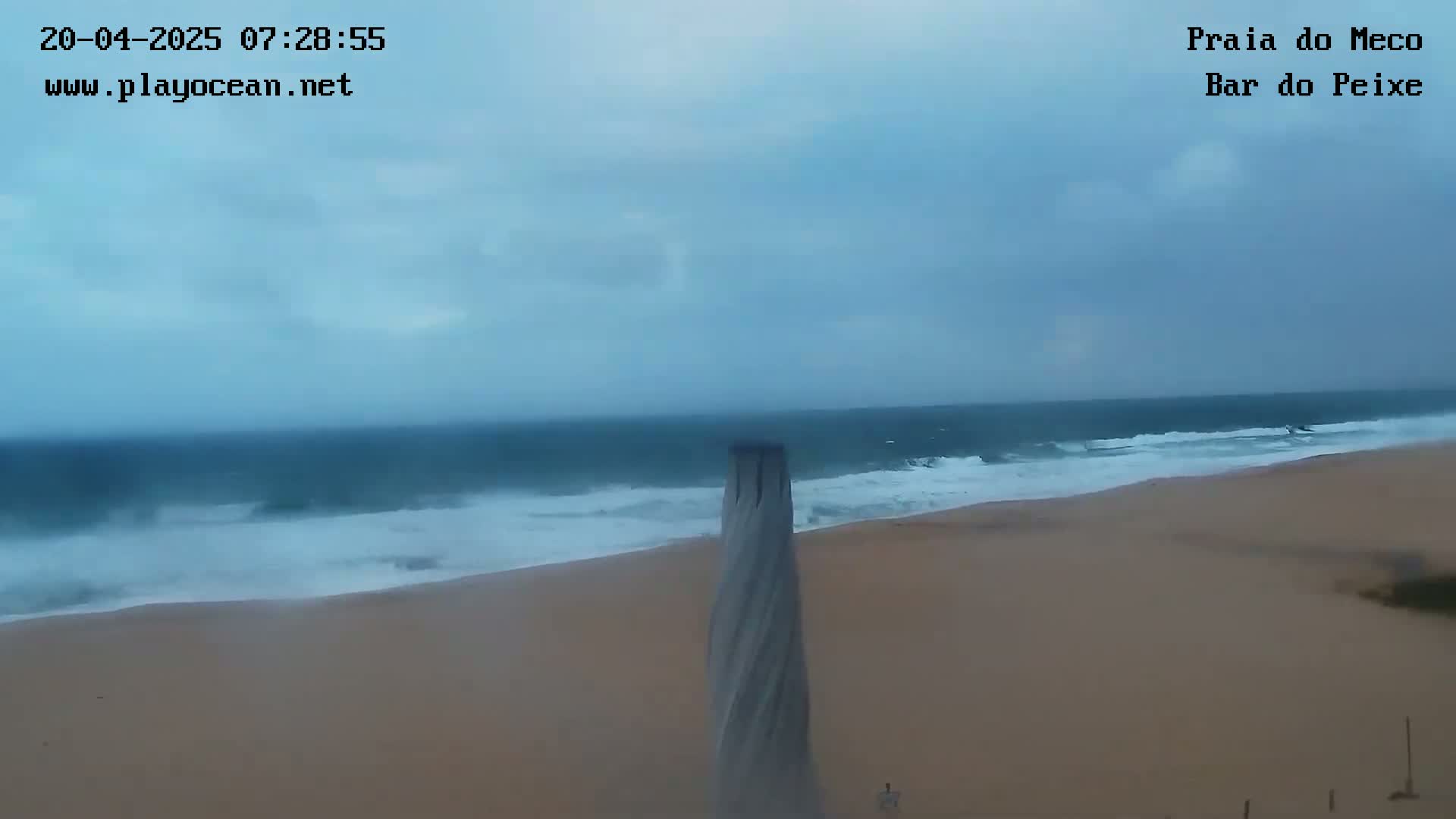 A sandy beach with moderate waves under an overcast sky is visible, with a tall, spiraling structure in the foreground.