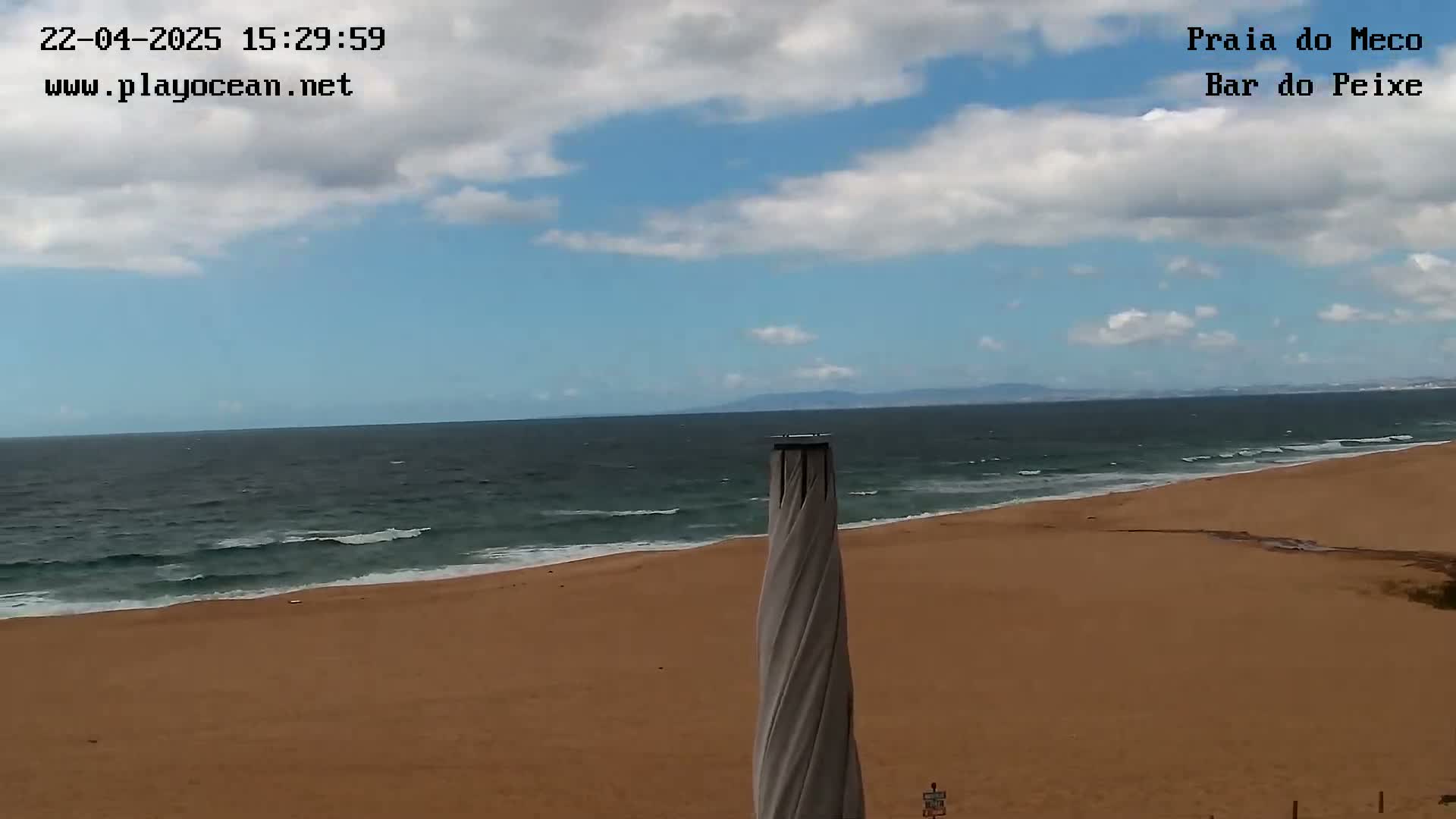 A sandy beach with a partly cloudy sky and a somewhat choppy ocean is shown, with a tall, slender object in the center.