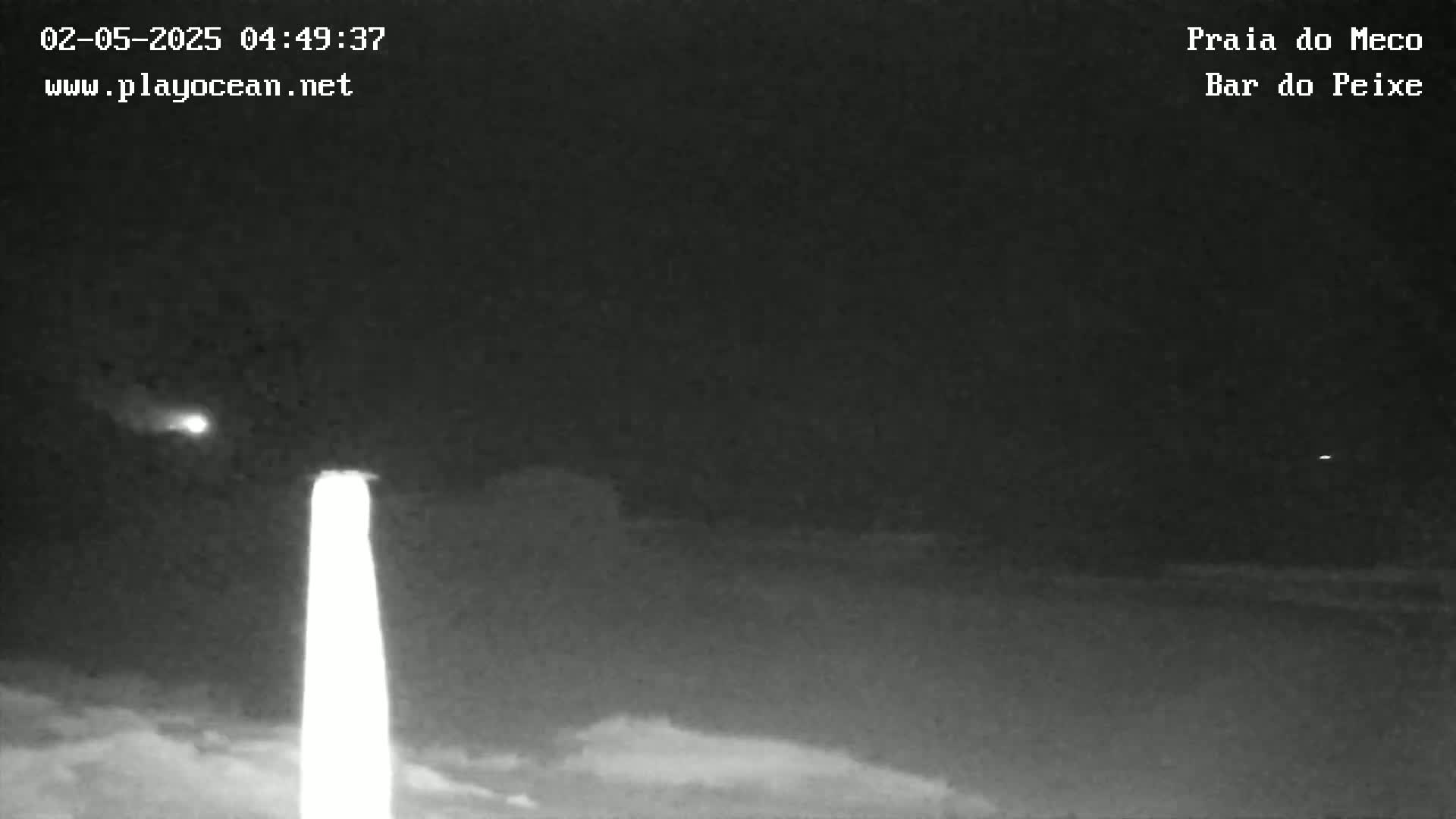 A nighttime, low-light image shows a bright light source in the lower-center, possibly a light post, with a dark, mostly featureless landscape visible in the background.