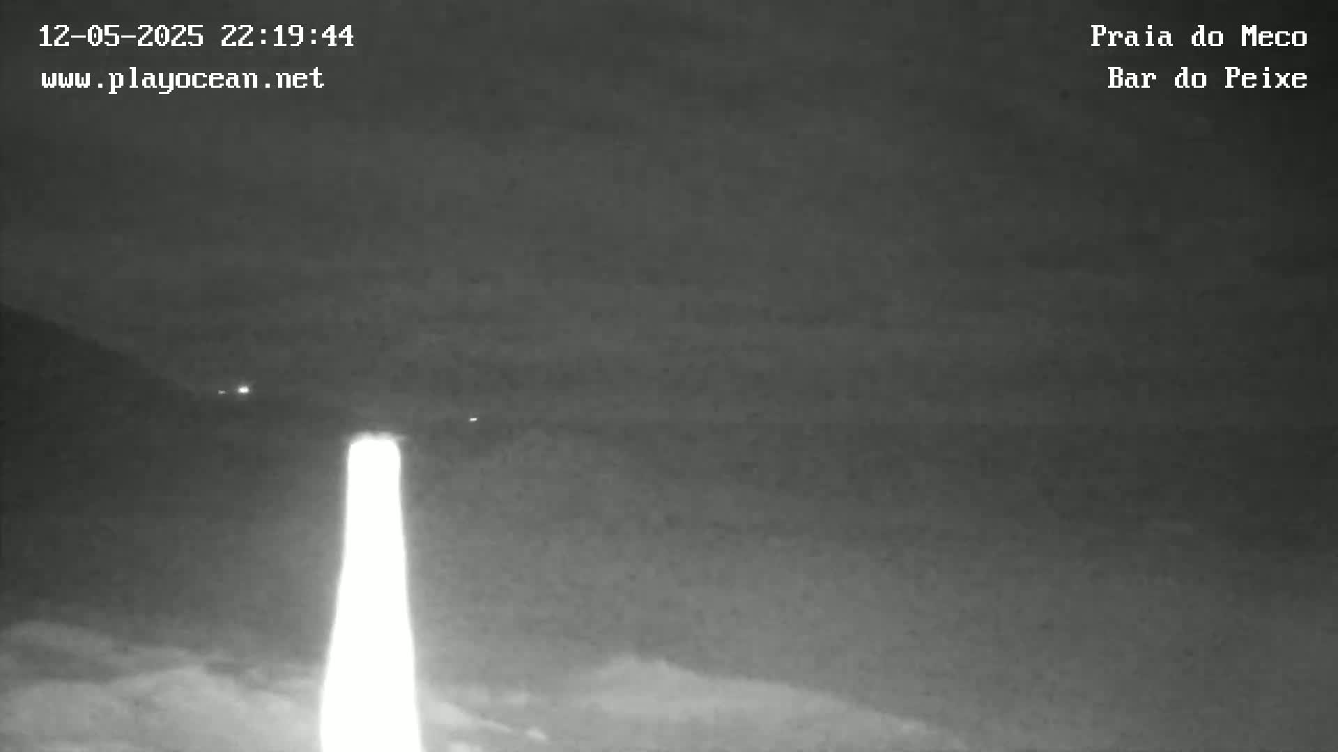 A bright light illuminates a dark, nighttime scene of what appears to be a beach or coastal area.