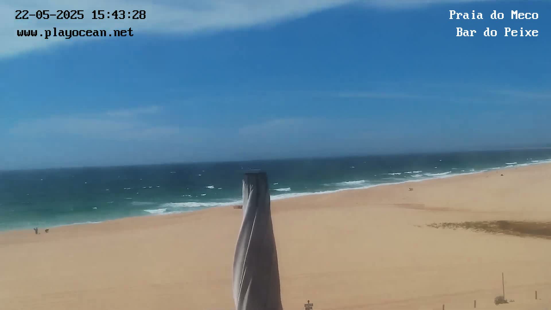 A sandy beach with a partly cloudy blue sky and a somewhat choppy ocean is visible from an elevated vantage point.