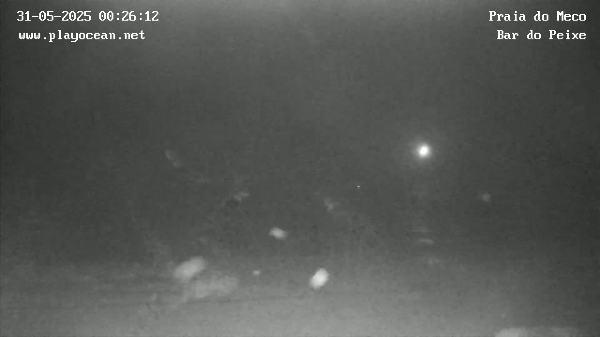 A low-light nighttime image shows a dark, indistinct scene with a few bright spots of light in the distance.