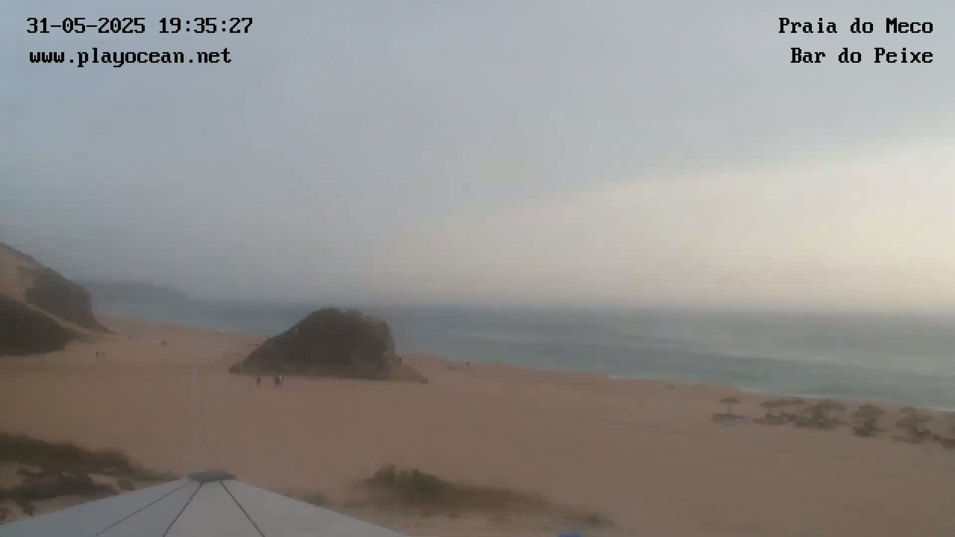 A hazy view of a sandy beach and ocean, with a few people visible on the beach.