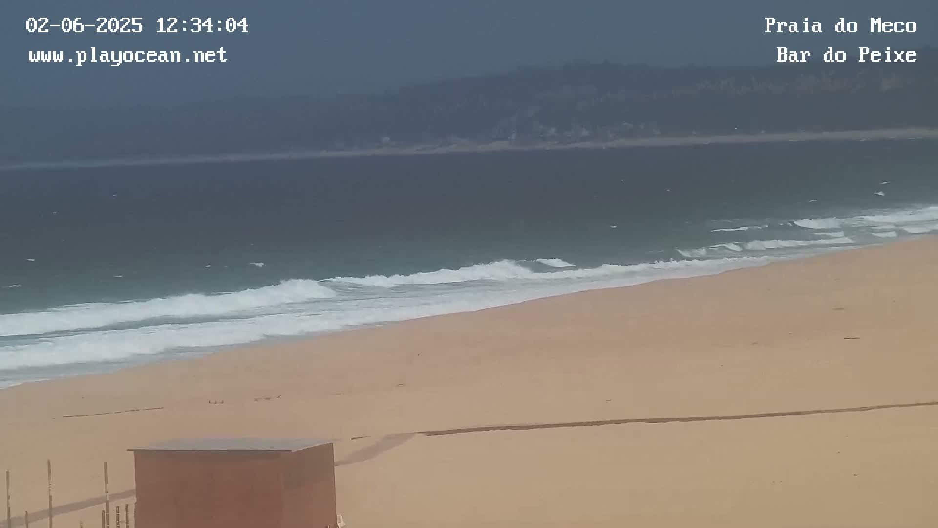 A sandy beach with moderate waves rolls onto the shore under an overcast sky.