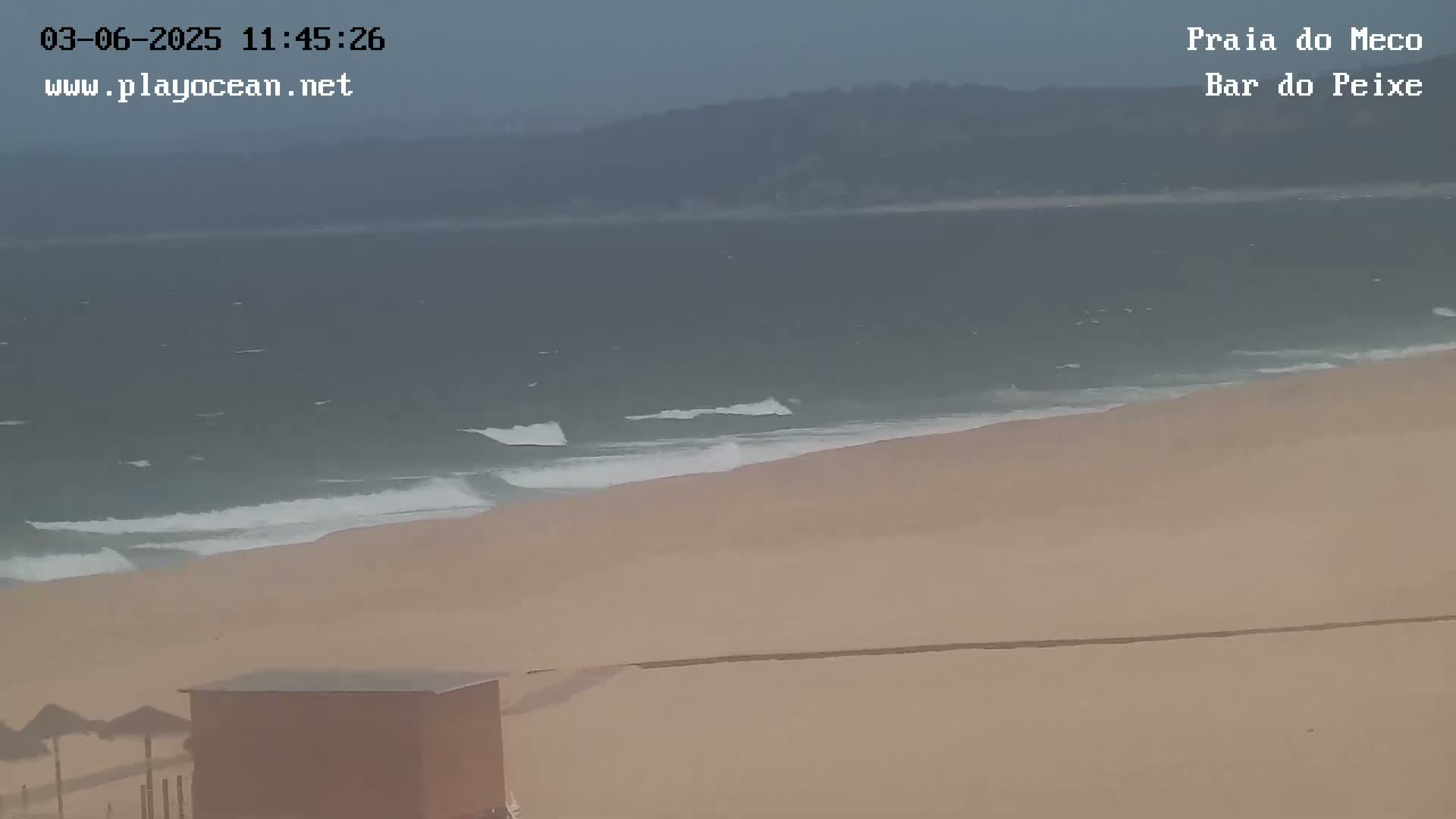 A sandy beach with small waves rolling onto the shore under an overcast sky.