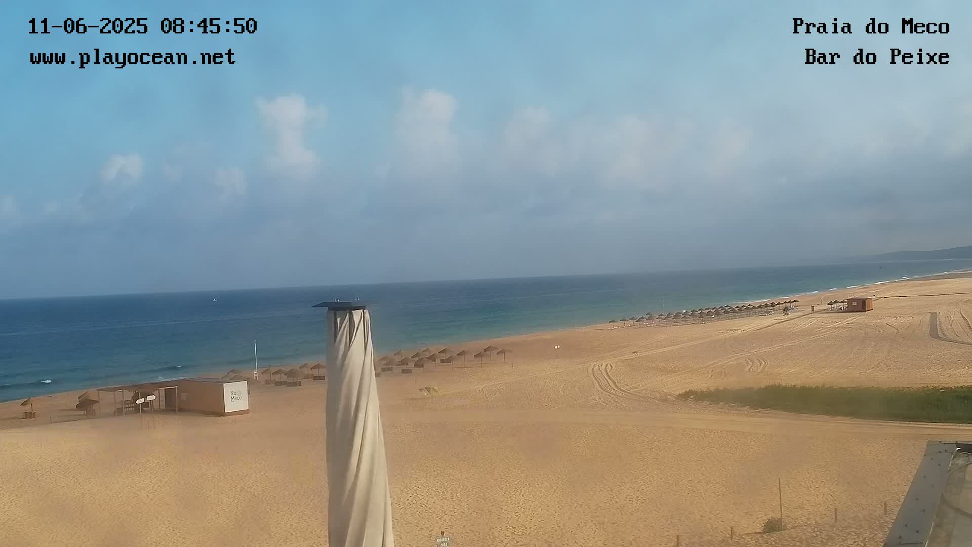 A partly cloudy day at a sandy beach with calm ocean waves and several beach umbrellas.