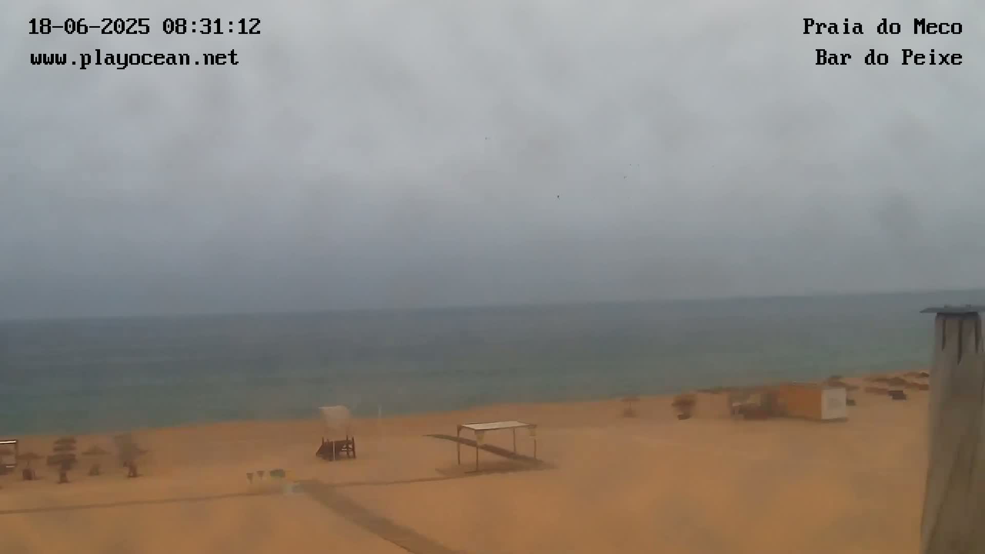 A mostly cloudy, overcast day shows a sandy beach with a few beach umbrellas and a calm ocean in the distance.