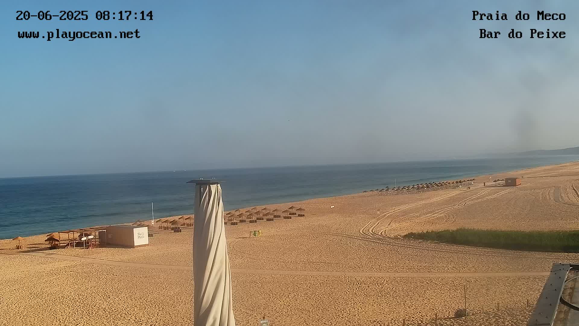 A sandy beach with scattered umbrellas stretches along a calm ocean under a clear sky.