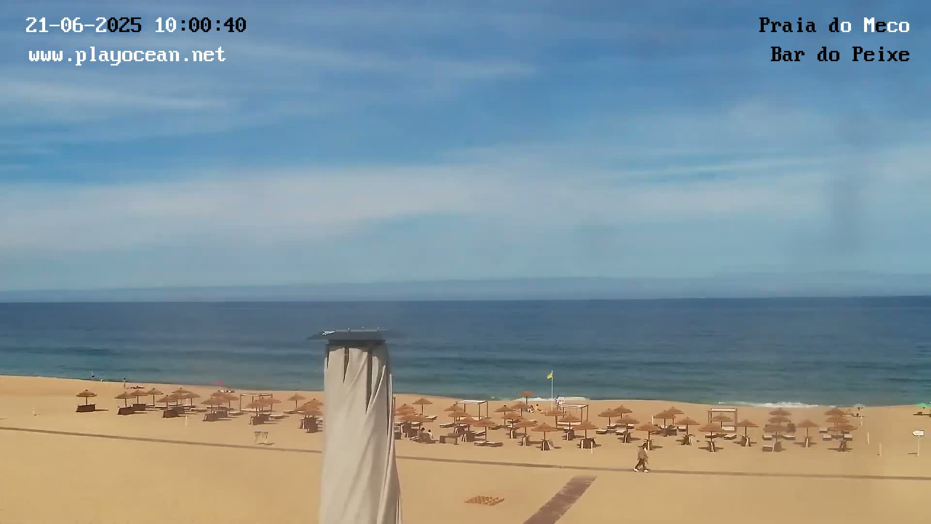 A sandy beach with numerous umbrellas and a calm ocean under a clear blue sky is visible from an elevated viewpoint.