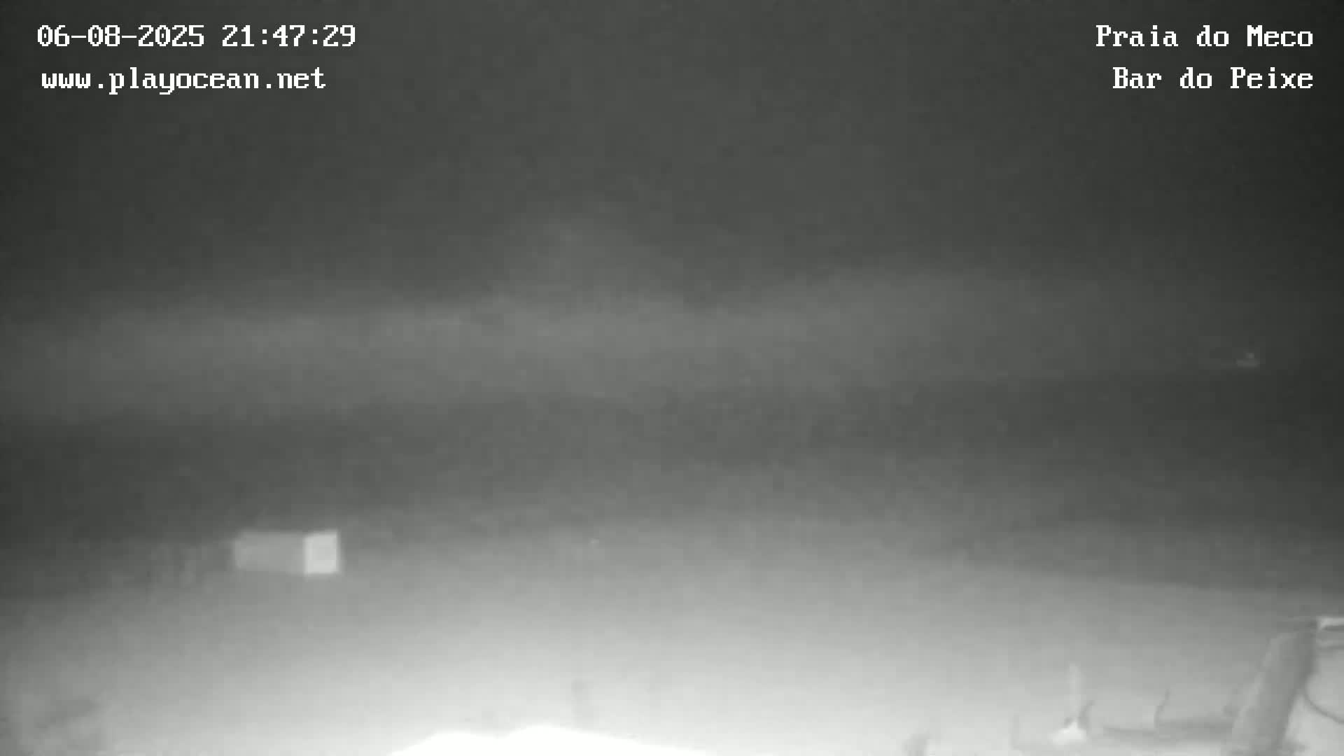 A nighttime, foggy or hazy scene shows a dark, indistinct landscape with a small structure visible in the lower left.