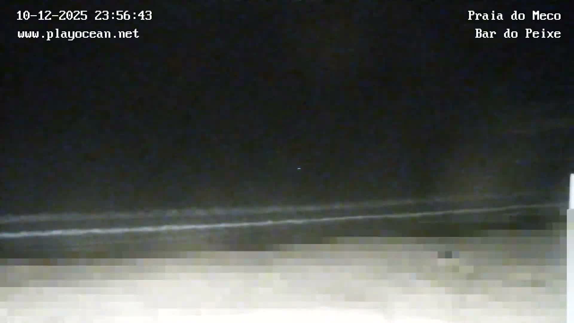 A very dark and pixelated outdoor night scene depicts a dimly discernible shoreline with faint horizontal lines, possibly waves, under a clear dark sky.
