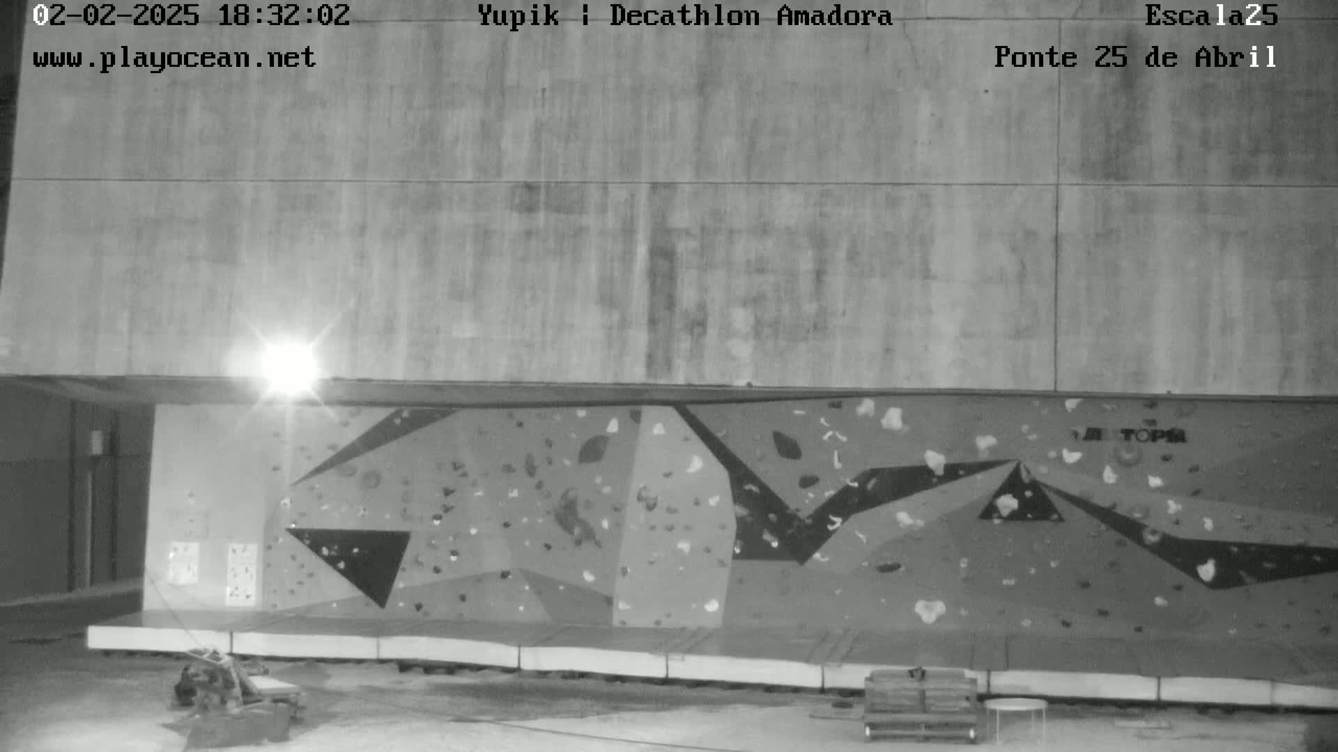 A nighttime, black and white view of an indoor climbing wall beneath a large concrete structure.