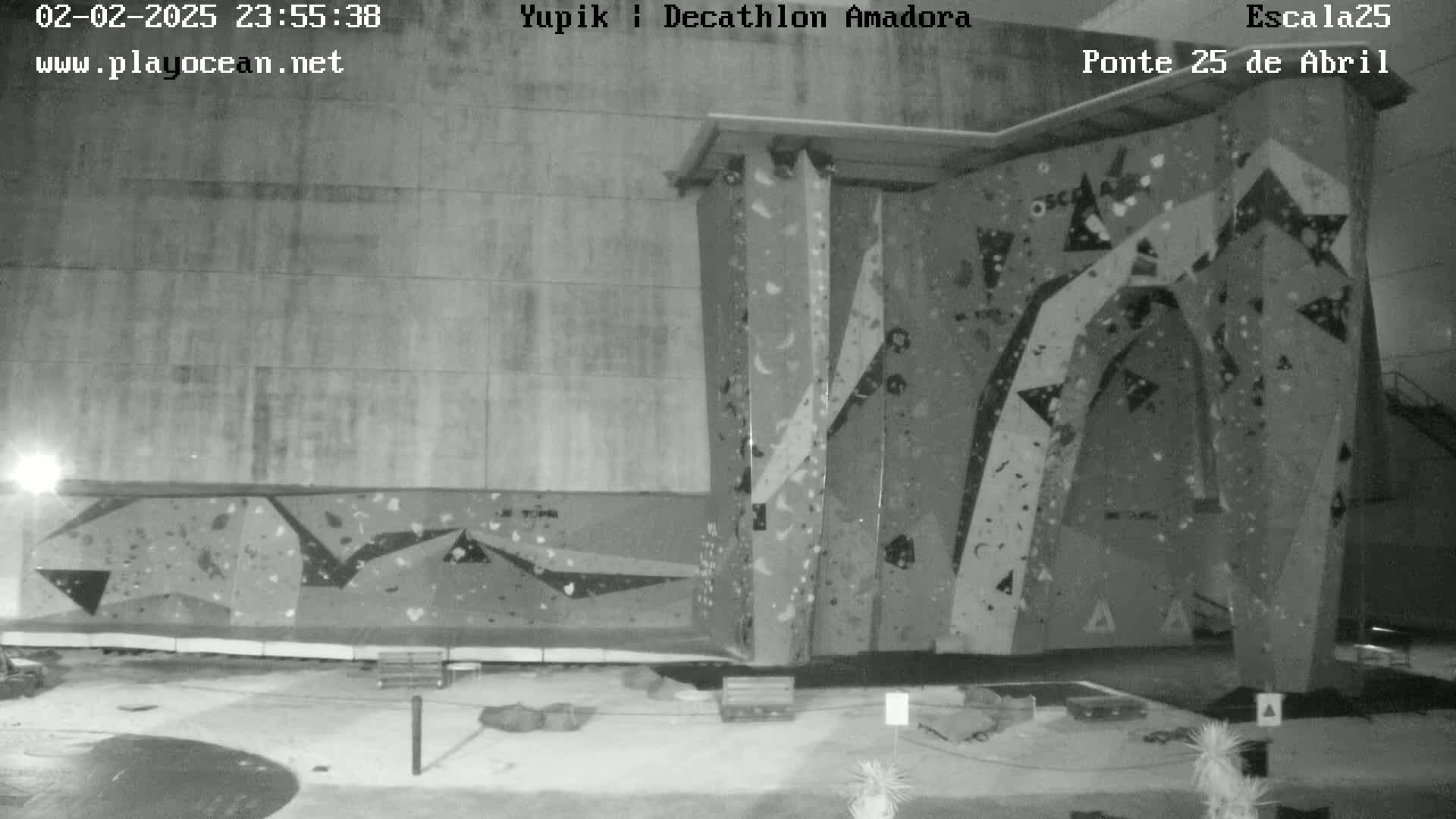 A black-and-white nighttime image shows an indoor climbing wall with various holds and features.