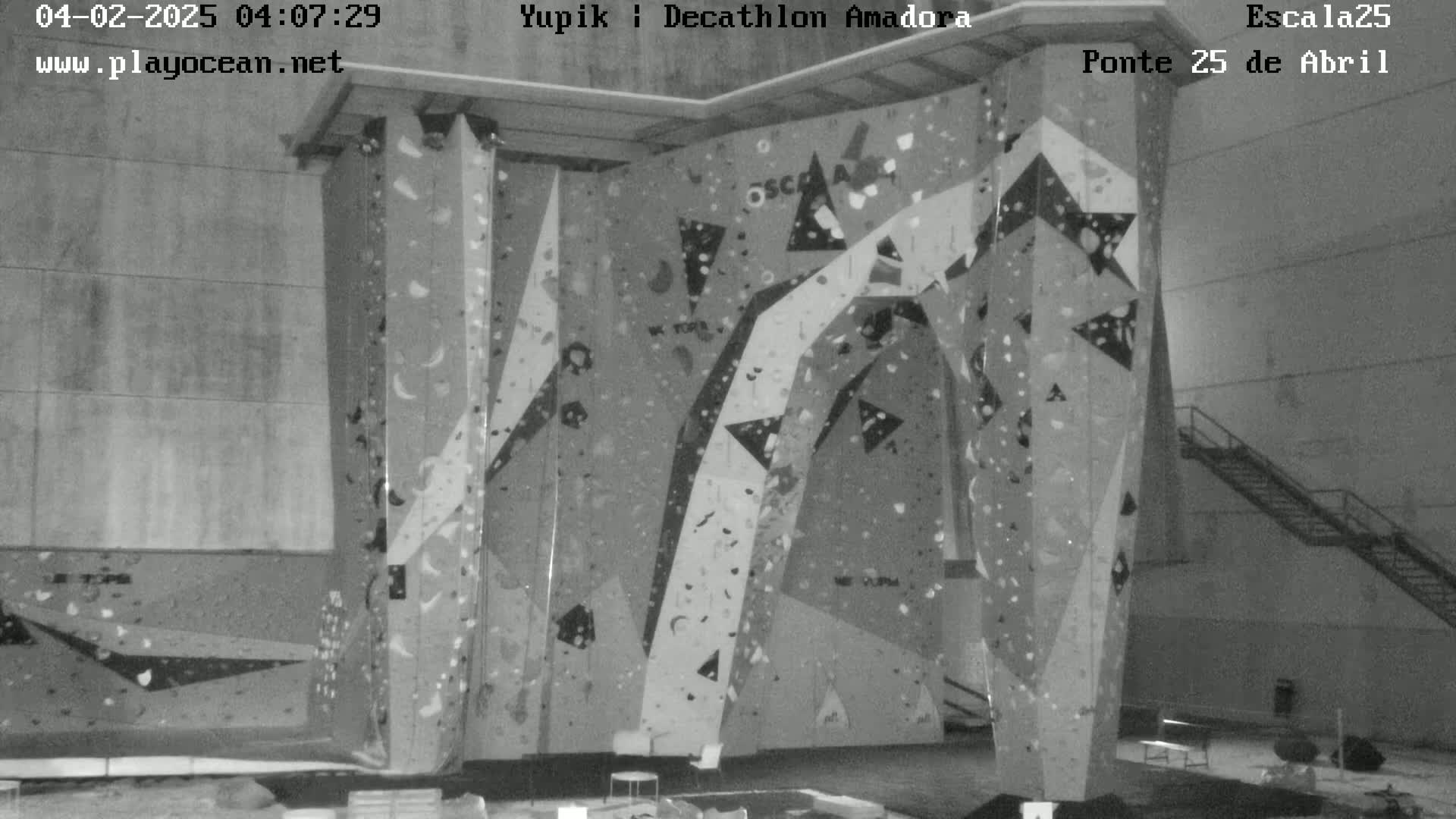 A grayscale image shows an indoor climbing wall with various holds and geometric designs.